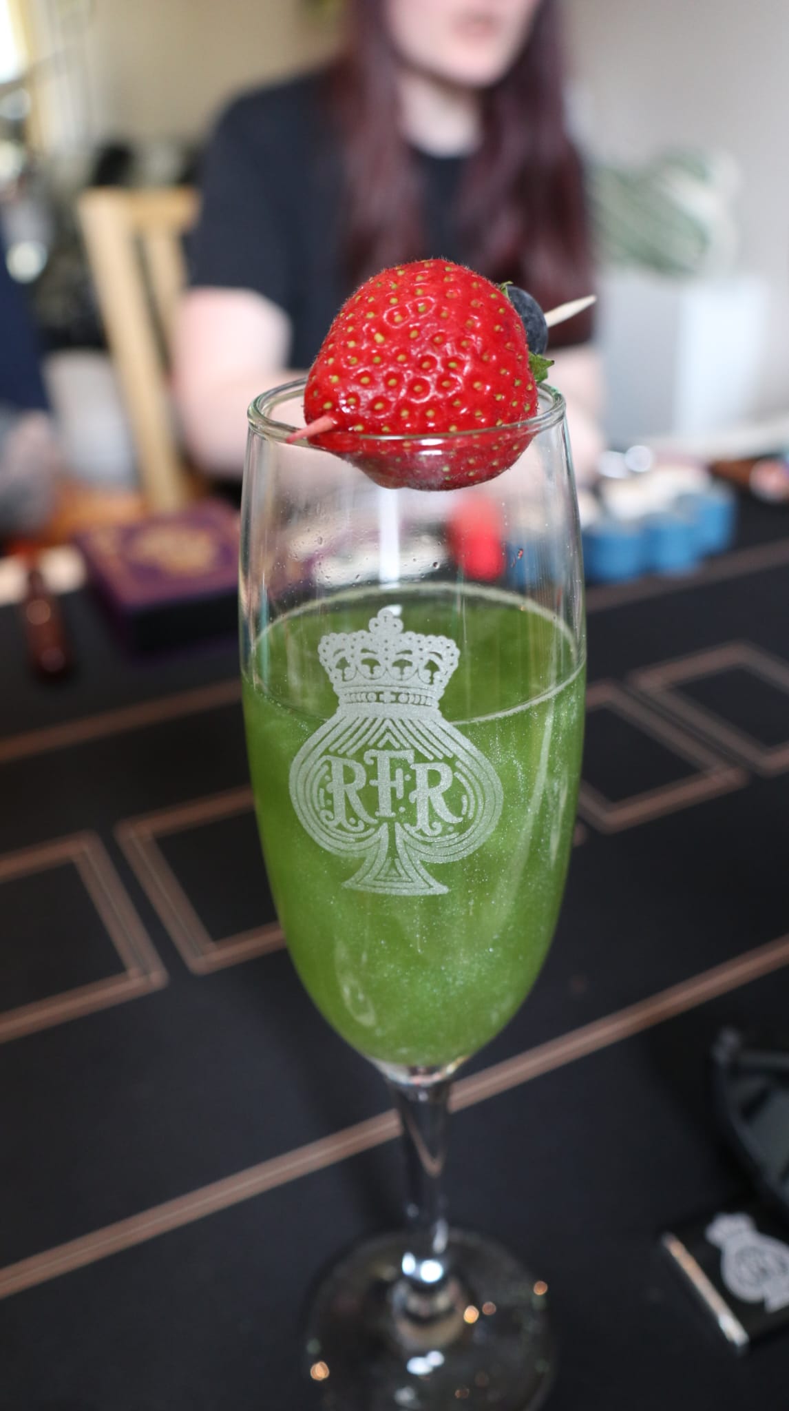 A green edible-glitter drink with a strawberry garnish in an engraved RFR glass